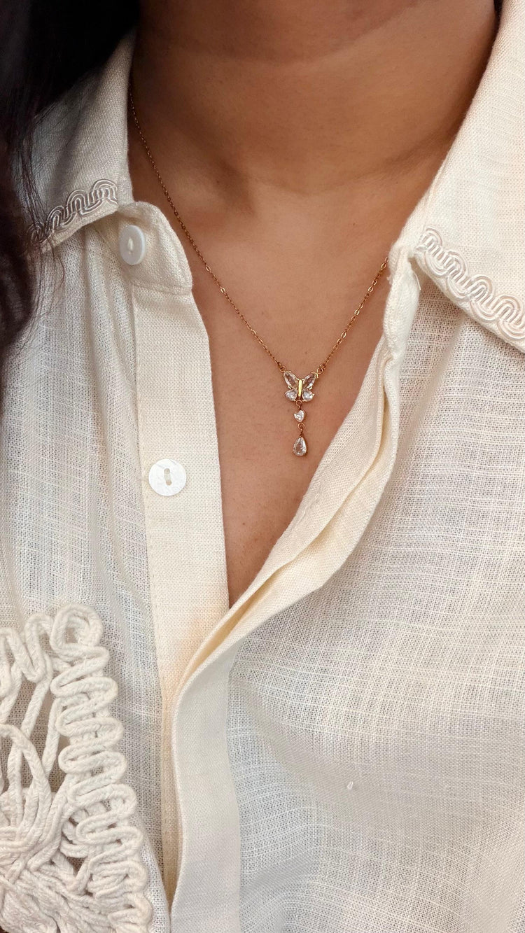 Gold butterfly drop necklace worn with a cream linen shirt